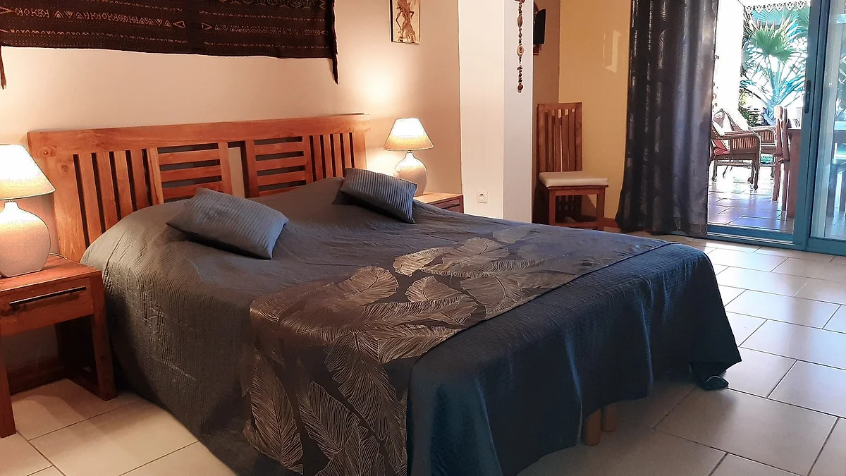 Une chambre double avec son lit en teck et la porte ouverte sur la terrasse