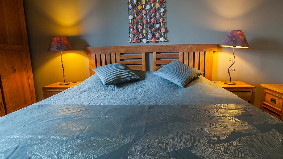 Le grand lit d'une chambre double, avec sa tête de lit en teck et ses lampes
