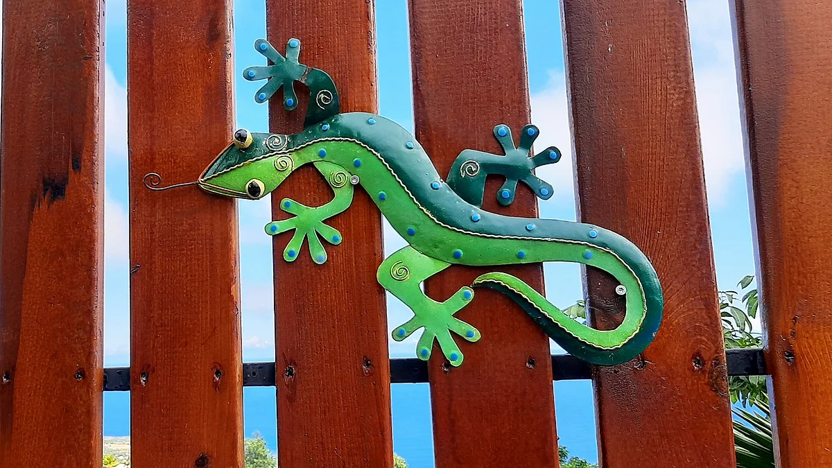 Un margouillat en métal coloré sur la palissade en bois