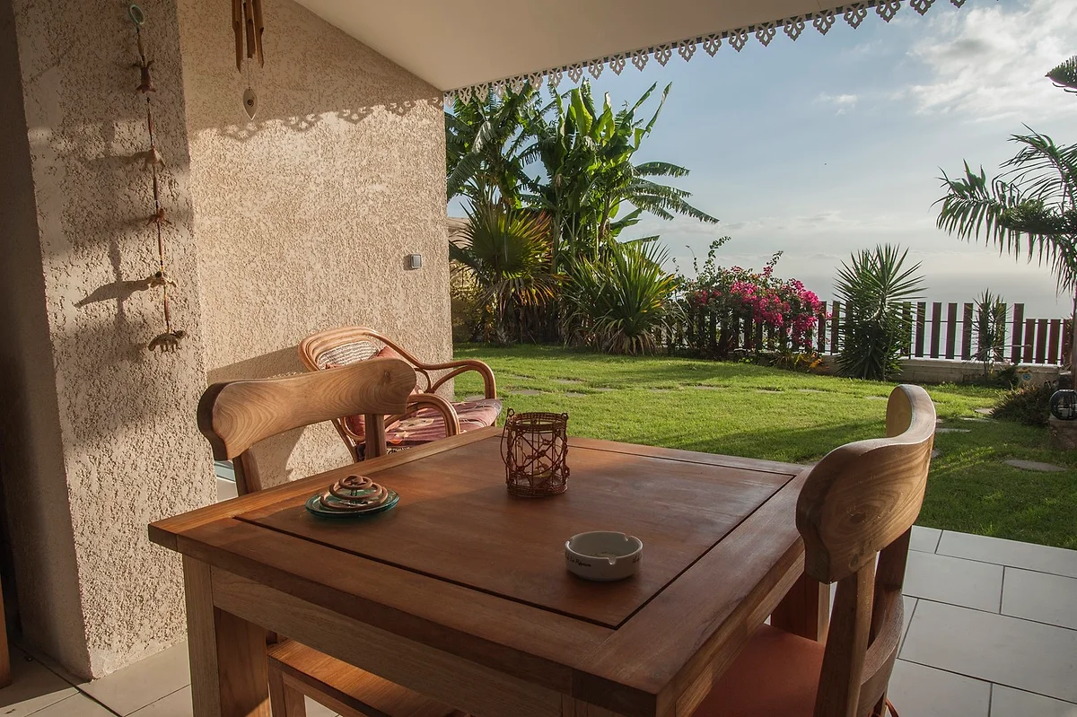 La terrasse couverte d'une chambre, sa table en bois et la vue sur le jardin